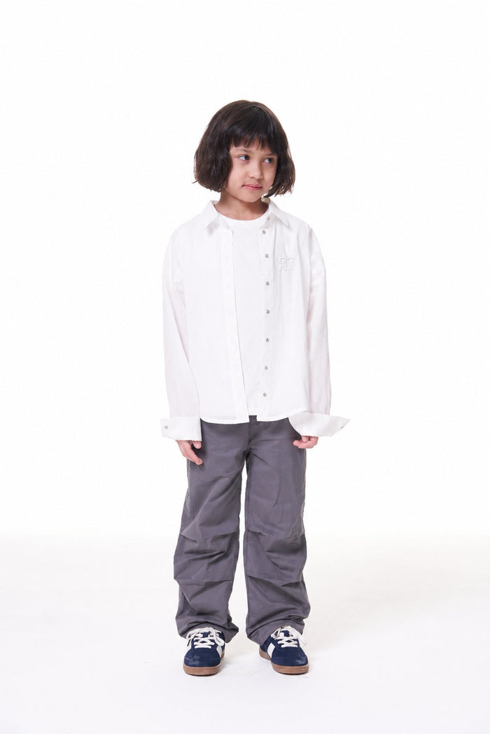 Girl wearing the ON7 Shirt in off white with grey trousers, full length